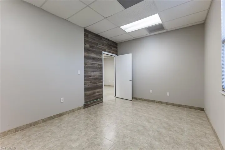Unfurnished room featuring a drop ceiling, wooden walls, and light tile patterned floors