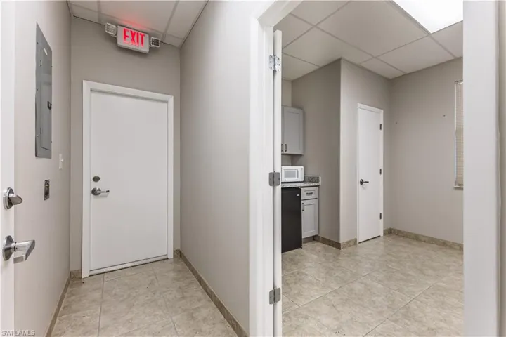 Corridor featuring light tile patterned flooring, a drop ceiling, and electric panel