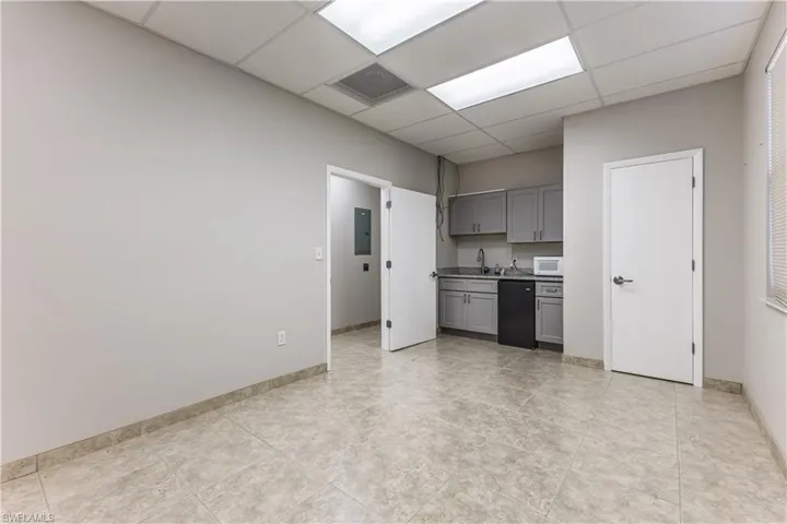 Kitchen with gray cabinets, a drop ceiling, electric panel, white microwave, and black dishwasher