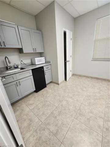 Kitchen featuring sink, dishwasher, a drop ceiling, and light tile floors