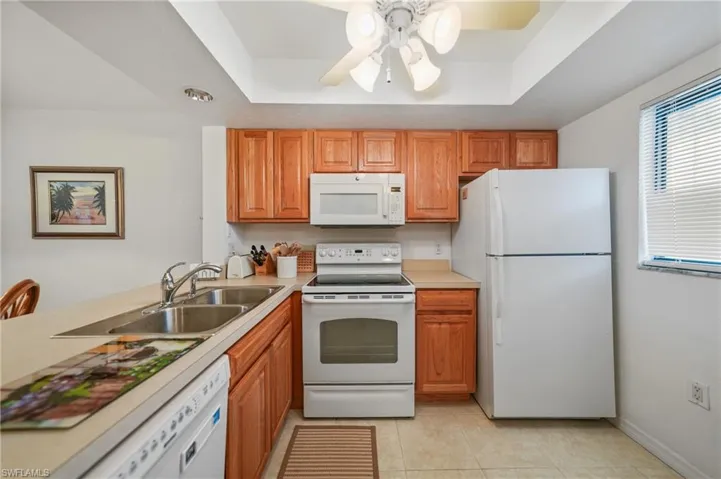 Kitchen with white appliances, light countertops, ceiling fan, and brown cabinetry