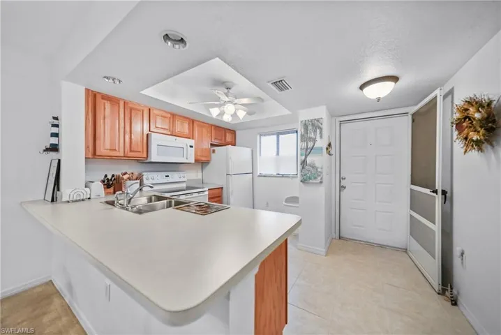 Kitchen with a peninsula, white appliances, light countertops, ceiling fan, and light tile patterned floors