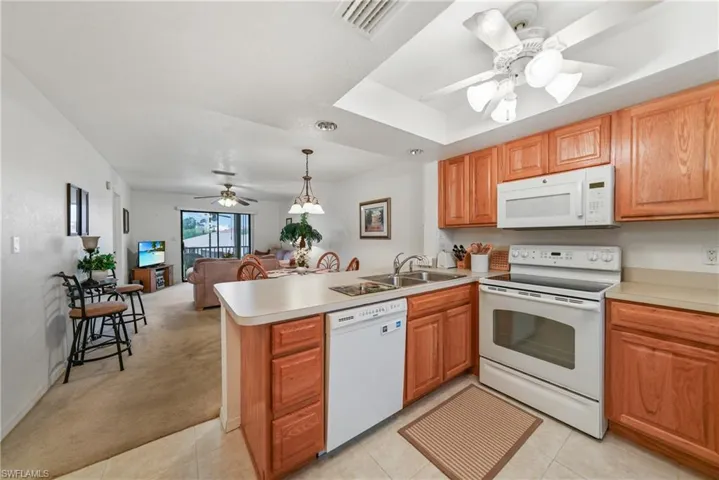 Kitchen featuring ceiling fan, white appliances, open floor plan, light countertops, and hanging light fixtures