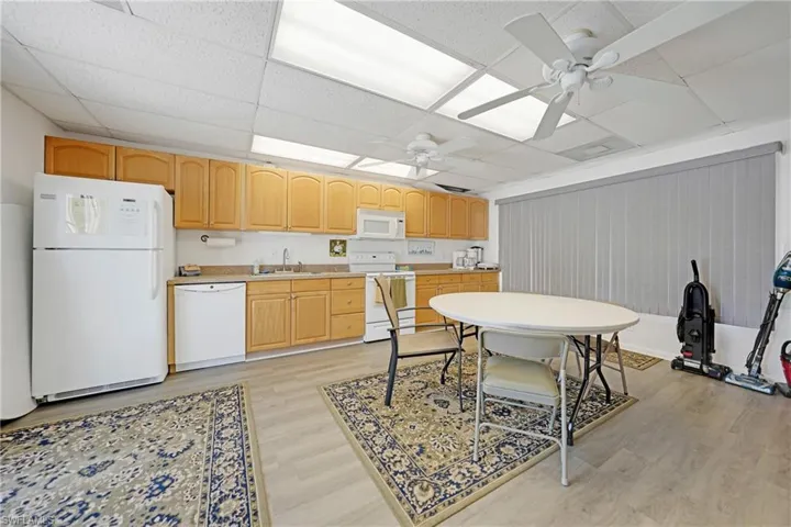 Kitchen with white appliances, light countertops, light brown cabinets, ceiling fan, and a drop ceiling
