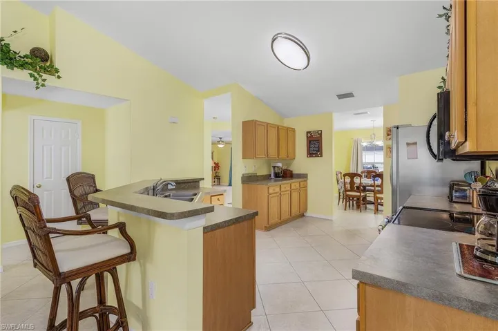 Kitchen with light tile flooring, kitchen peninsula, a kitchen breakfast bar, sink, and electric stove