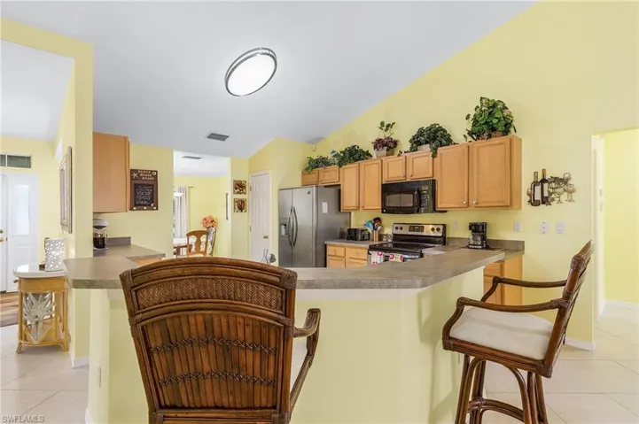 Kitchen with kitchen peninsula, a kitchen bar, appliances with stainless steel finishes, light tile floors, and lofted ceiling