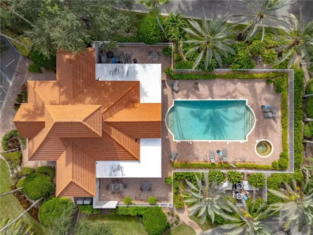 Aerial perspective of a multi-faceted tile roof featuring a screened-in pool, integrated spa, paved patio area, and mature perimeter landscaping