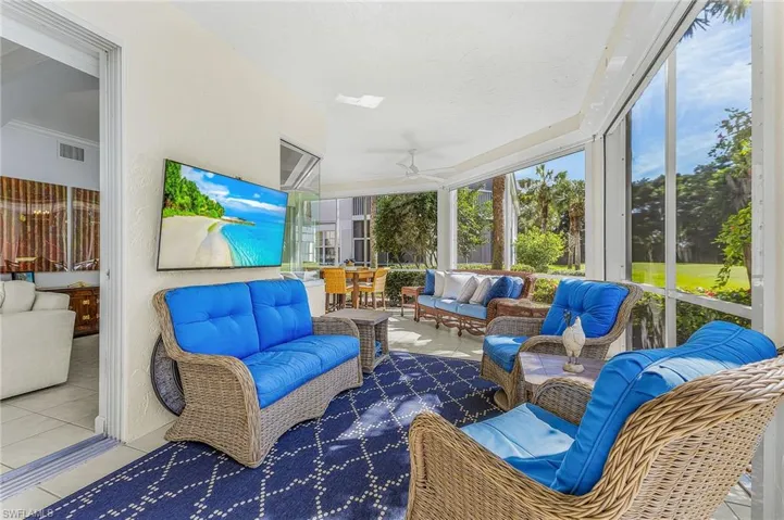 Screened lanai featuring tile flooring, ceiling fan, wall-mounted television, and exterior landscaping