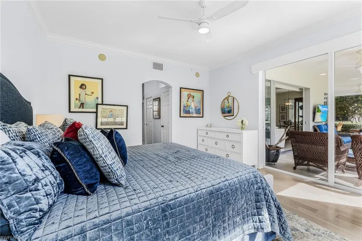 Interior room featuring wood-finish flooring, a white ceiling fan with integrated lighting, a crown-molded perimeter, an arched entryway, and sliding glass doors