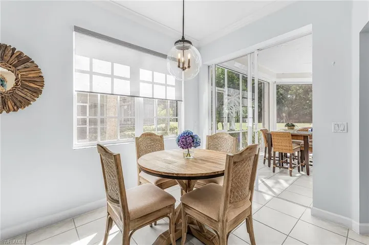 Sun-filled breakfast area featuring large grid-pattern windows, sleek ceramic tile flooring, and a contemporary glass globe pendant light, with access to a screened-in lanai through sliding glass doors