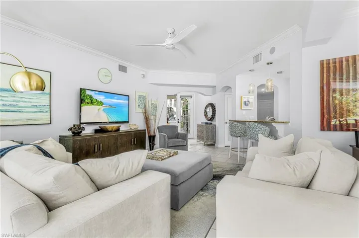 Open-concept interior featuring crown molding, neutral tile flooring, a white three-blade ceiling fan, and a built-in breakfast bar with pendant lighting