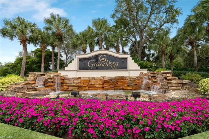 Monument entrance featuring stacked stone water features, professional landscaping with flowering shrubs, and mature palm trees