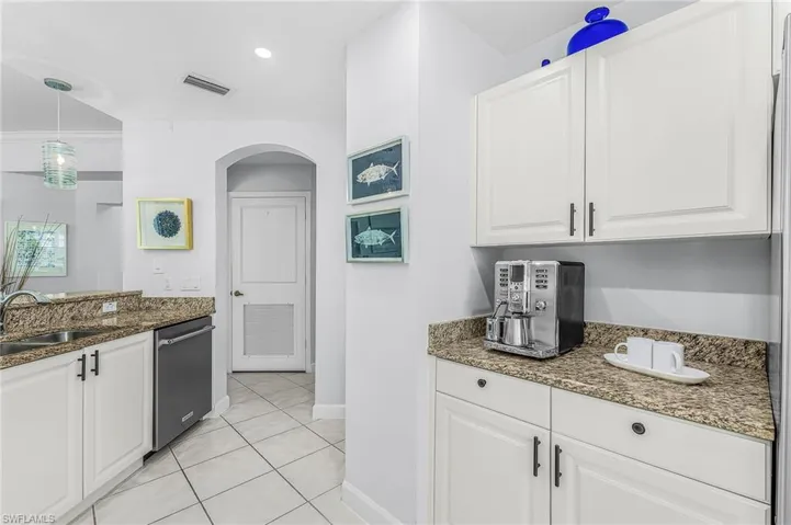 Kitchen featuring white shaker-style cabinetry, speckled stone countertops, a stainless steel dishwasher, tile flooring, and an arched doorway