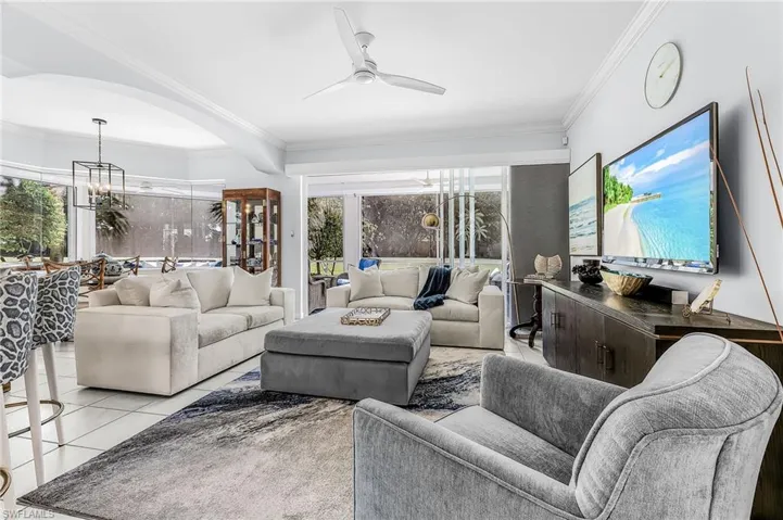 Open-concept living area featuring neutral tile flooring, crown molding, a central ceiling fan, and sliding glass wall panels
