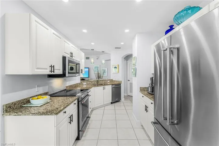 Kitchen featuring white shaker-style cabinetry with matte black hardware, stone countertops, stainless steel appliances, and tile flooring