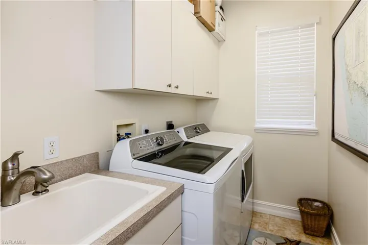 Clothes washing area featuring tile patterned flooring, a sink, baseboards, washer and dryer, and cabinet space