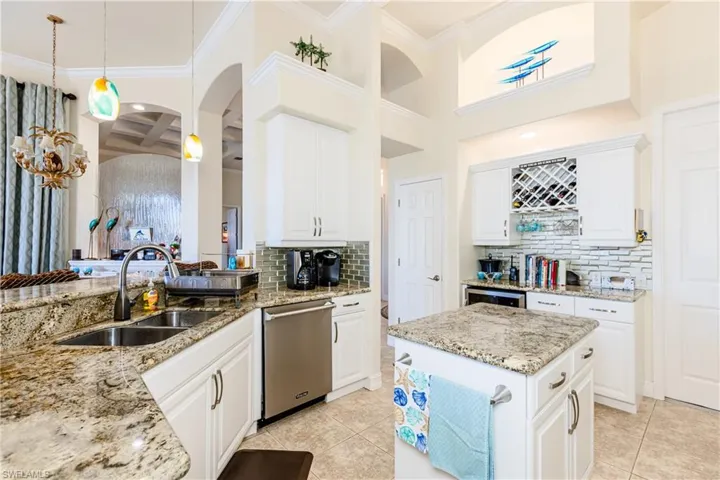 Kitchen with light tile patterned floors, a sink, white cabinets, light stone countertops, and dishwasher