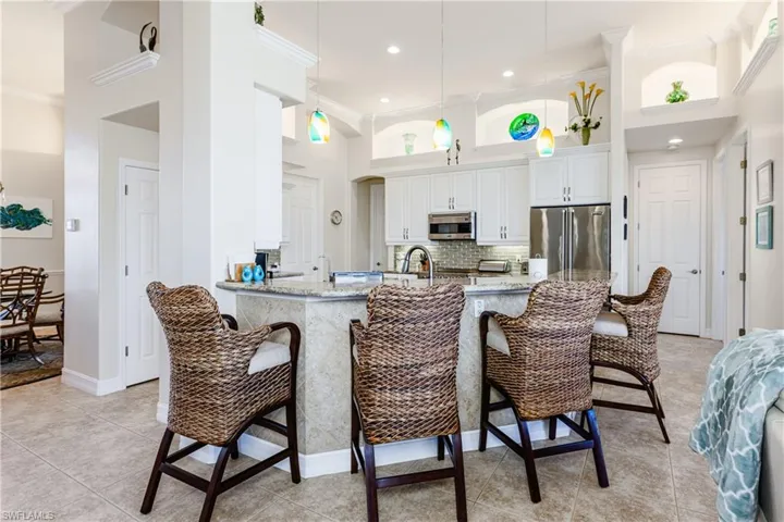 Kitchen featuring a towering ceiling, ornamental molding, appliances with stainless steel finishes, light stone countertops, and a kitchen bar