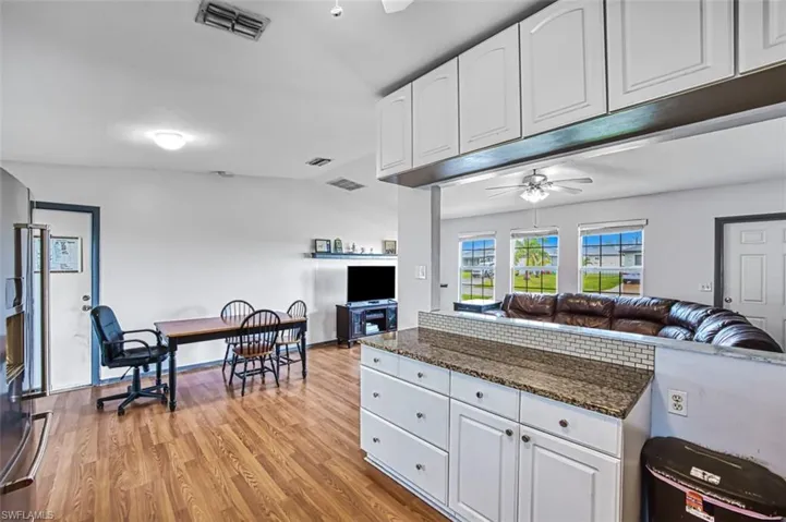 Kitchen with ceiling fan, light hardwood / wood-style flooring, dark stone countertops, white cabinets, and lofted ceiling