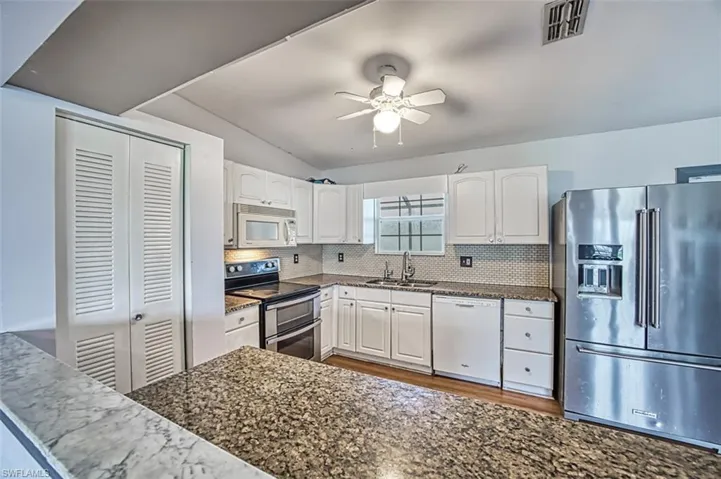 Kitchen with dark stone counters, tasteful backsplash, stainless steel appliances, sink, and white cabinetry