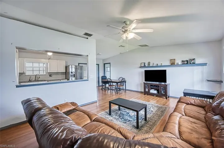 Living room featuring sink, lofted ceiling, light wood-type flooring, and ceiling fan