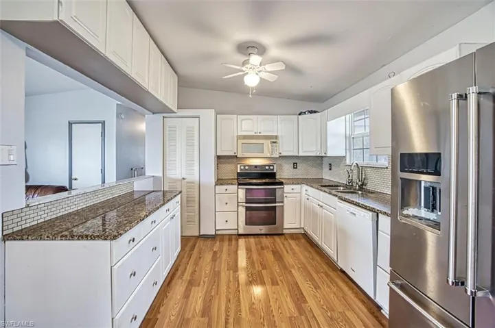 Kitchen with light hardwood / wood-style floors, tasteful backsplash, white cabinetry, appliances with stainless steel finishes, and sink