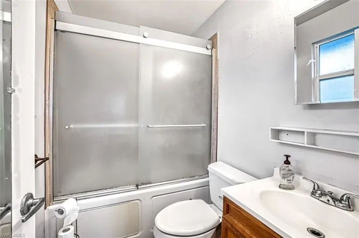 Full bathroom with enclosed tub / shower combo, vanity, and toilet