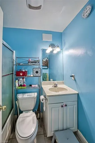 Full bathroom featuring enclosed tub / shower combo, tile floors, oversized vanity, and toilet