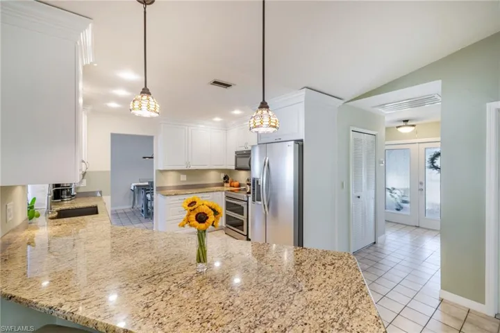 Kitchen with a peninsula, light tile patterned floors, stainless steel appliances, light stone counters, and lofted ceiling