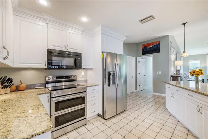 Kitchen featuring stainless steel appliances, white cabinets, light stone counters, light tile patterned floors, and recessed lighting