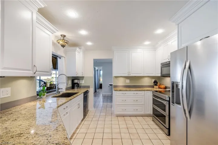Kitchen featuring stainless steel and black appliances, light tile patterned floors, white cabinetry, light stone countertops, and recessed lighting