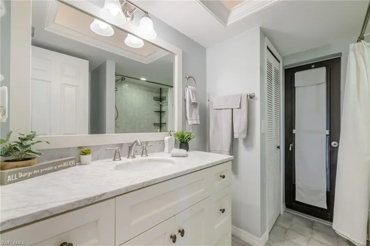 Bathroom featuring a closet, vanity, light tile patterned flooring, and tiled shower
