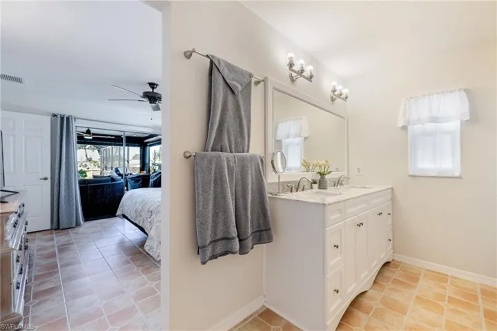 Ensuite bathroom featuring double vanity, light tile patterned floors, and a ceiling fan