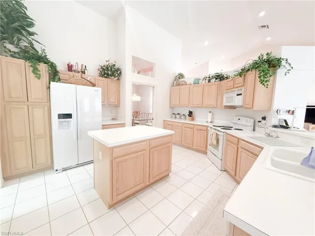 Kitchen with light brown cabinetry, sink, a center island, light tile patterned floors, and white appliances