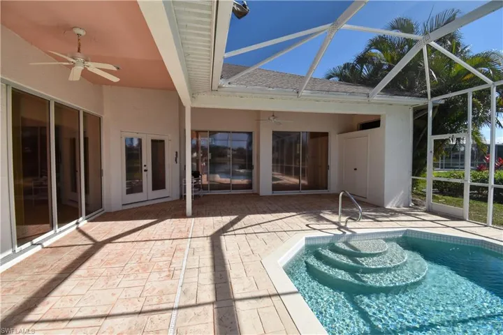 View of swimming pool featuring glass enclosure, a patio area, ceiling fan, and french doors