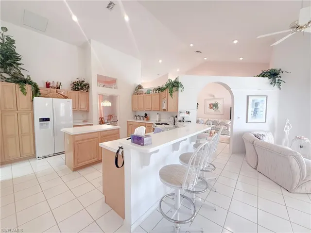 Kitchen featuring a kitchen island, lofted ceiling, a breakfast bar area, white refrigerator with ice dispenser, and kitchen peninsula