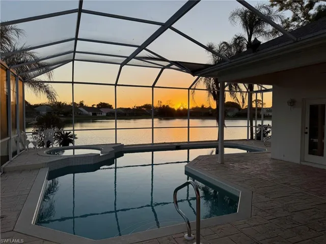 Pool at dusk featuring a water view, an in ground hot tub, a lanai, and a patio area