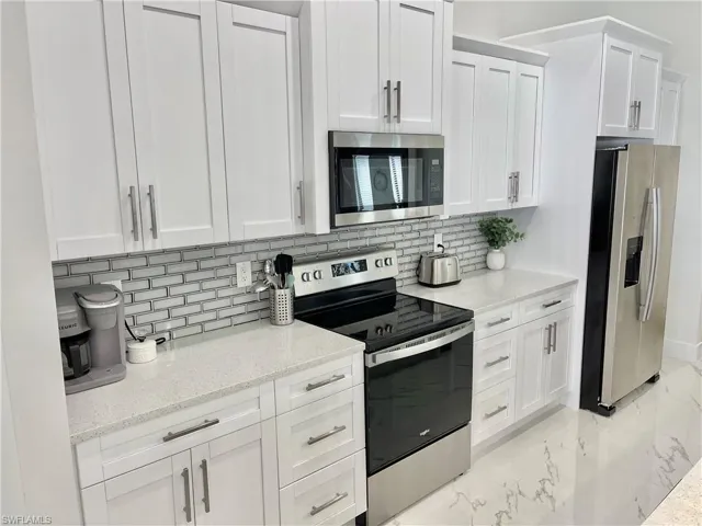Kitchen featuring white cabinetry, appliances with stainless steel finishes, light stone counters, and decorative backsplash