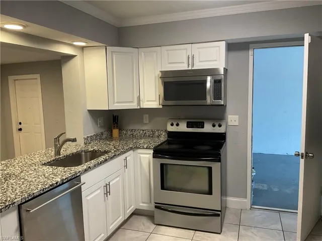 Kitchen with white cabinetry, appliances with stainless steel finishes, stone countertops, sink, and light tile flooring