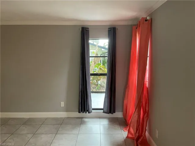 Tiled empty room featuring crown molding
