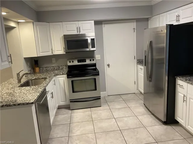 Kitchen featuring sink, light stone counters, white cabinetry, and appliances with stainless steel finishes
