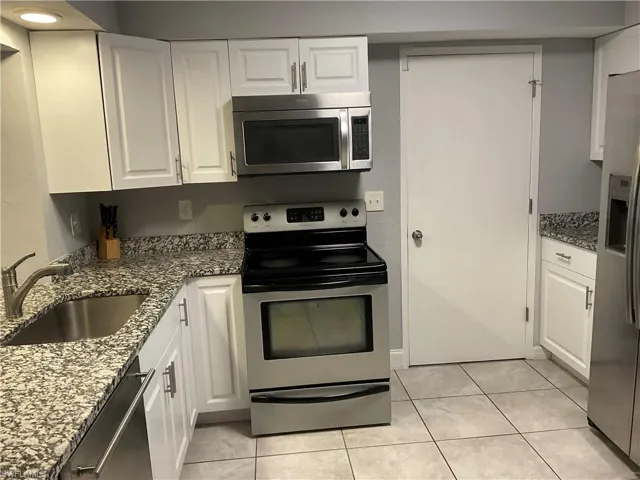 Kitchen with sink, white cabinets, light tile floors, and stainless steel appliances