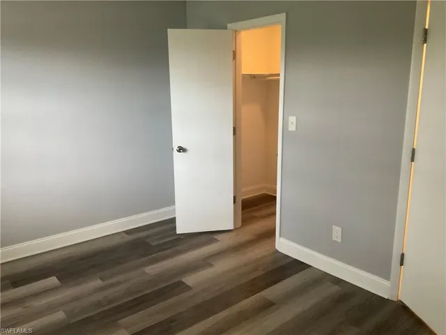 Unfurnished bedroom with a closet, a walk in closet, and dark wood-type flooring