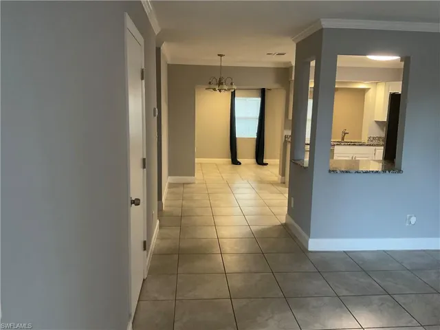 Corridor with a notable chandelier, ornamental molding, and light tile floors