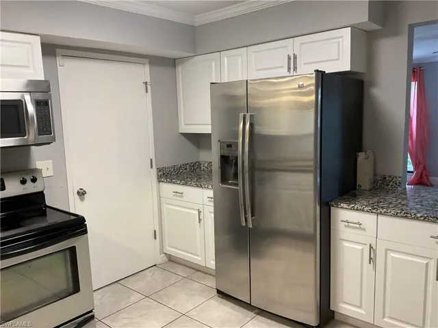 Kitchen with white cabinetry, ornamental molding, stainless steel appliances, dark stone counters, and light tile flooring