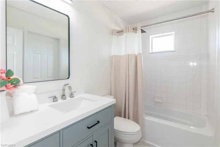 Bathroom featuring a light blue vanity with a white countertop, modern rectangular mirror, a shower-over-tub combination, and white square wall tiling