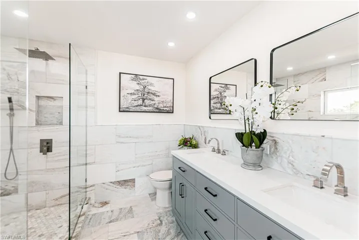 Bathroom with double vanity, a marble finish shower, tile walls, recessed lighting, and a wainscoted wall
