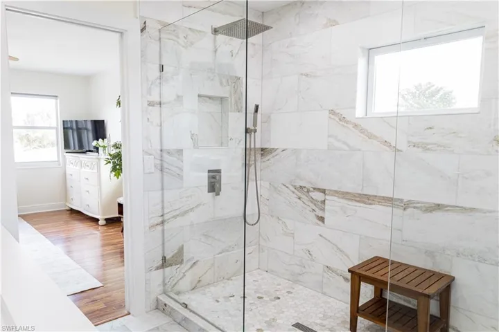 Glass-enclosed shower featuring large format tile with natural veining, a rainfall showerhead, and a built-in niche