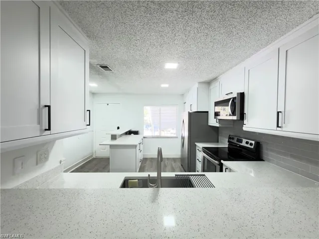 Modern kitchen featuring white shaker cabinetry, stainless steel appliances, speckled white countertops, a sleek subway tile backsplash, and a large undermount sink with a gooseneck faucet