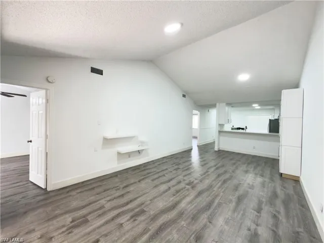 Spacious interior featuring wood-finish flooring, vaulted ceilings, recessed lighting, and a kitchen pass-through with white cabinetry
